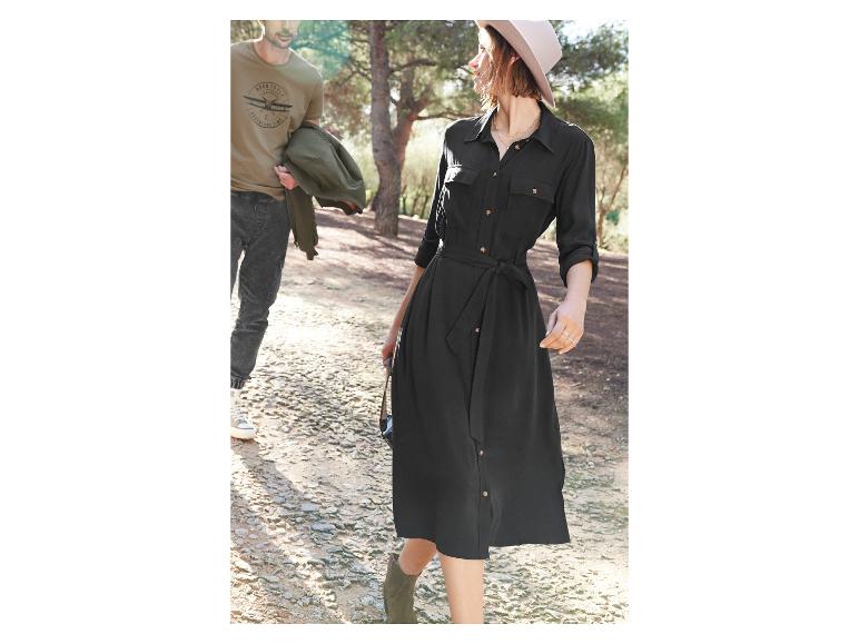 Een vrouw draagt een zwarte jurk met ceintuur en een hoed, terwijl een man een T-shirt met een vliegtuigprint draagt.