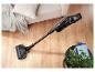 Aspirateur balai sans fil avec fonction de nettoyage sur parquet à côté d'un canapé et d'une plante.