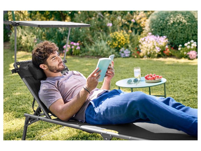 Homme se détend sur une chaise longue de jardin avec pare-soleil, lisant un livre.