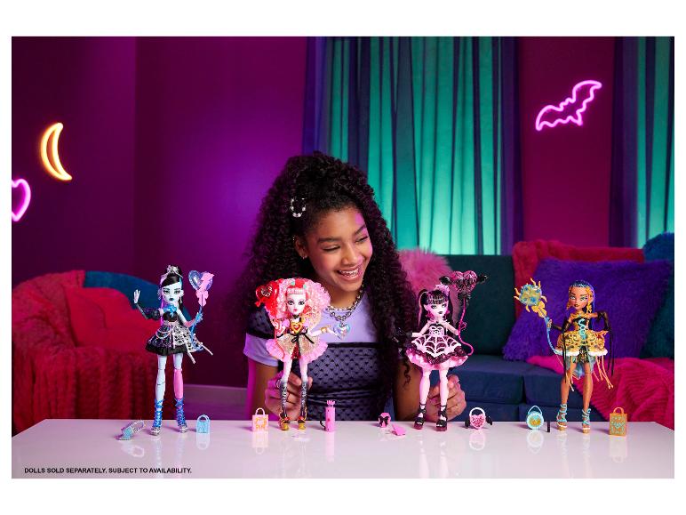 Une fille souriante tient des poupées Monster High, avec d'autres poupées et accessoires sur une table.