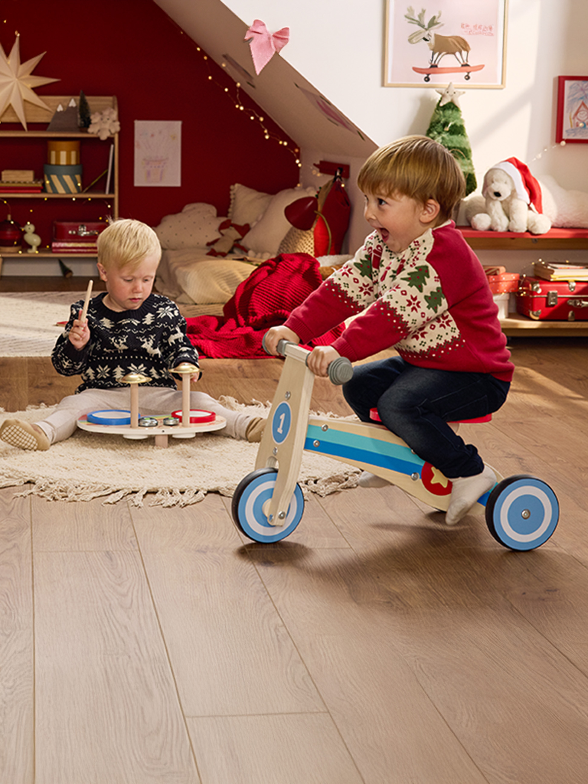 Deux enfants jouent avec des jouets en bois dans une chambre décorée pour Noël.