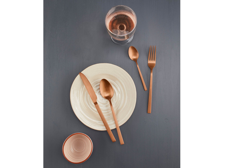 Een bord, mes, vork en lepel in koperen kleur op een donkergrijze tafel