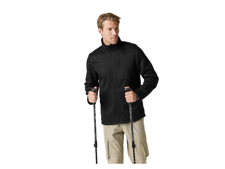 Homme en veste polaire noire et pantalon cargo beige tenant des bâtons de randonnée.