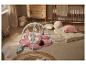 Baby op roze speelmat met speelboog, omringd door kinderkamerdecoratie.
