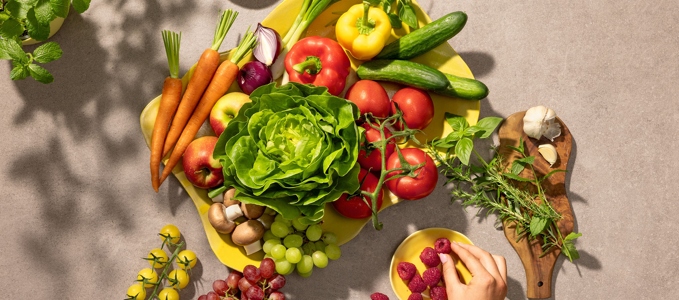 Verse groenten en fruit op een gele schaal, waaronder sla, tomaten, wortels en bessen.