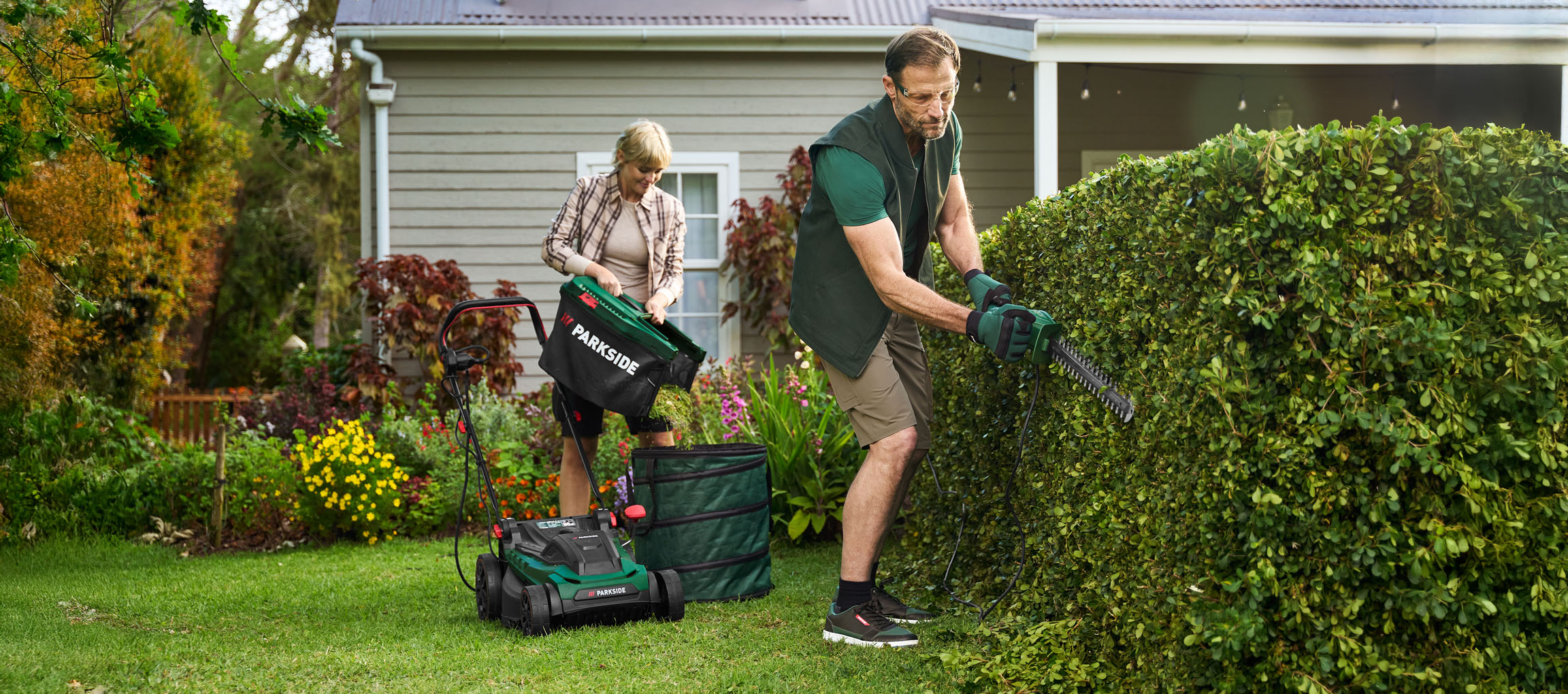 Homme taille haie, femme vide tondeuse à gazon dans le jardin.