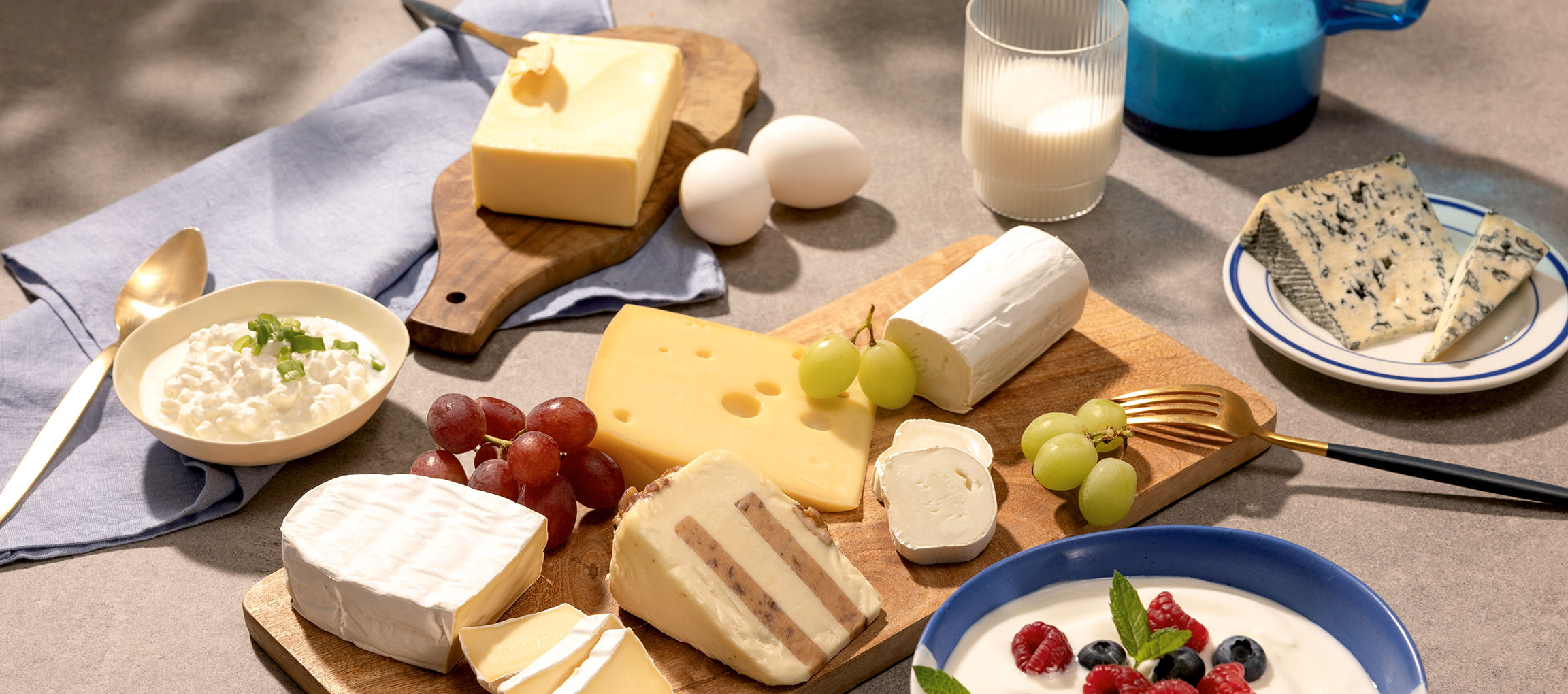 Diverse kazen, eieren, druiven, melk en yoghurt met bessen op een tafel.