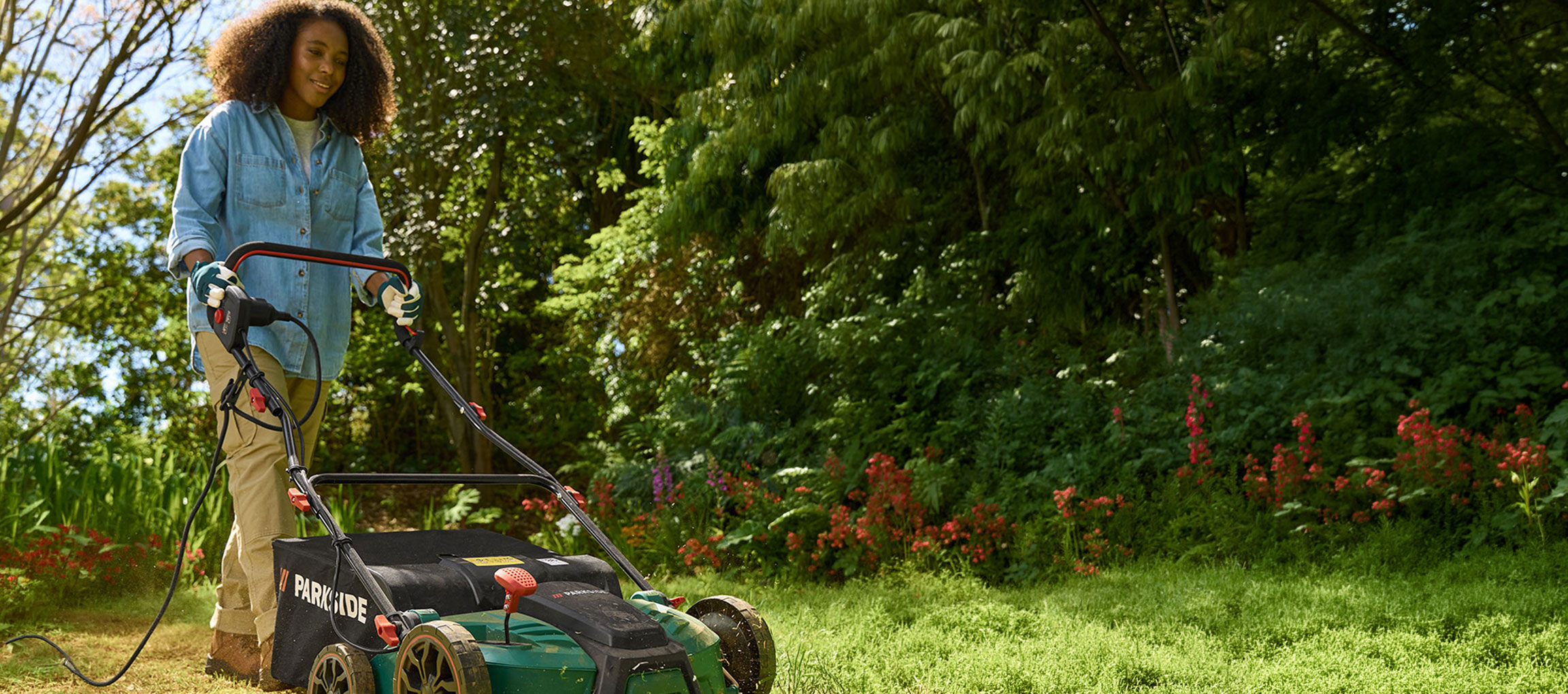 Femme dans un jardin utilisant une tondeuse à gazon électrique.