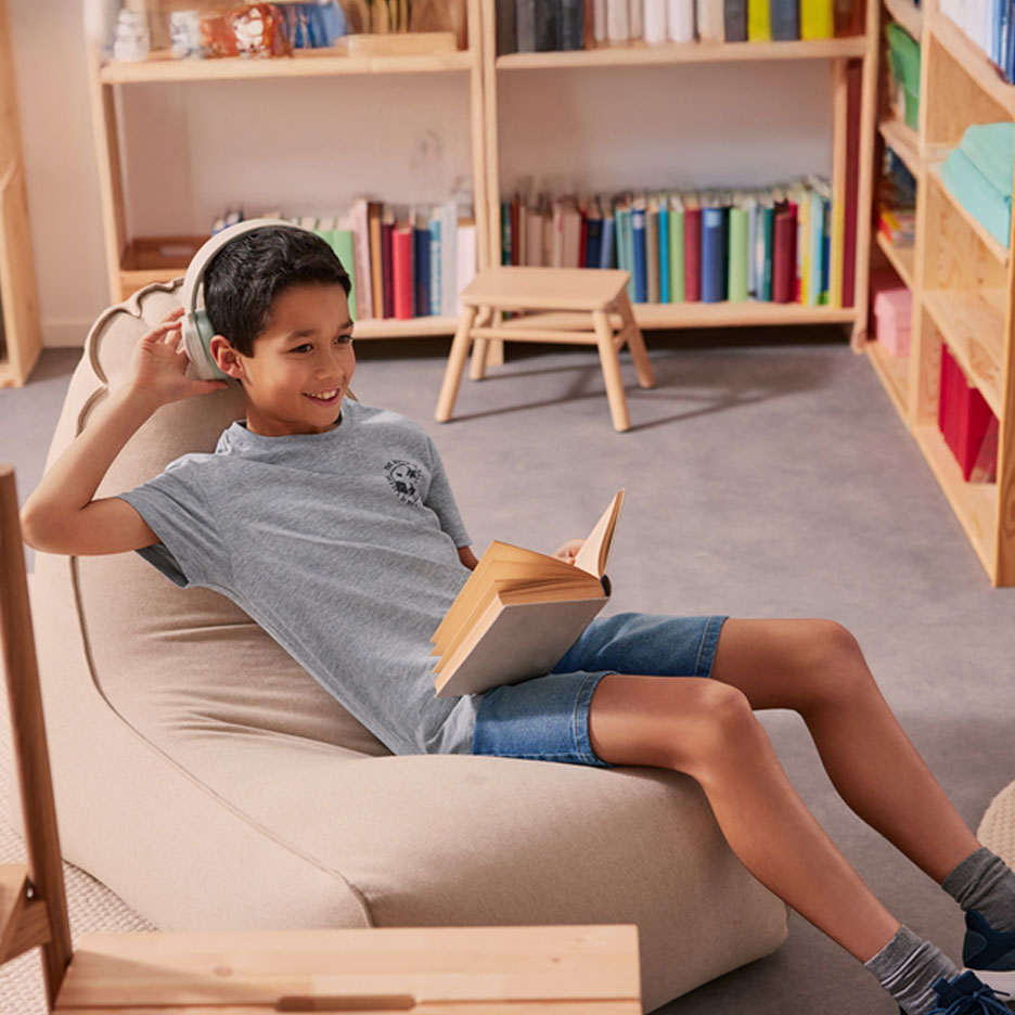 Jongetje met koptelefoon leest een boek in een zachte fauteuil.