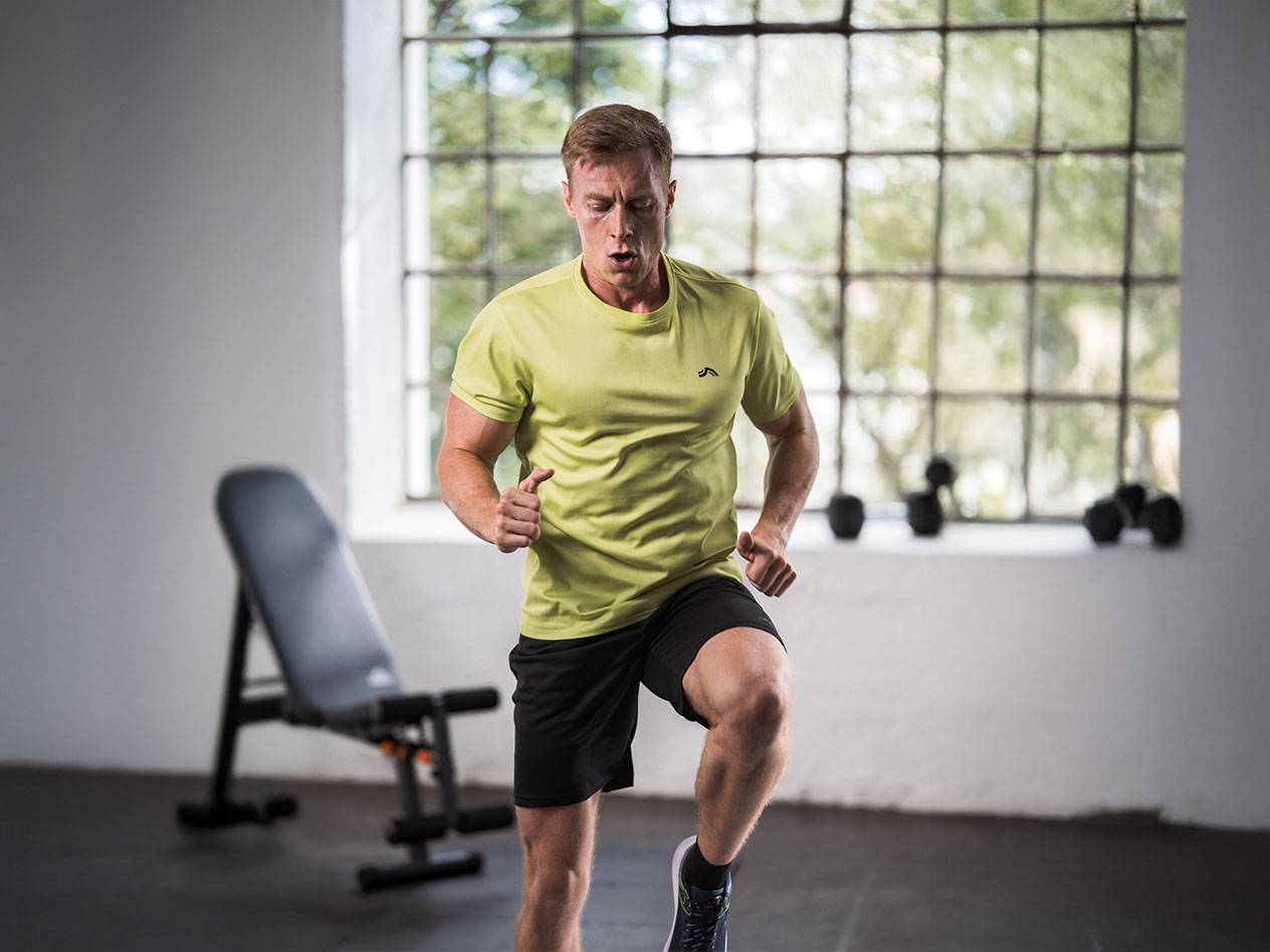 Homme en t-shirt jaune et short noir courant dans une salle de sport.