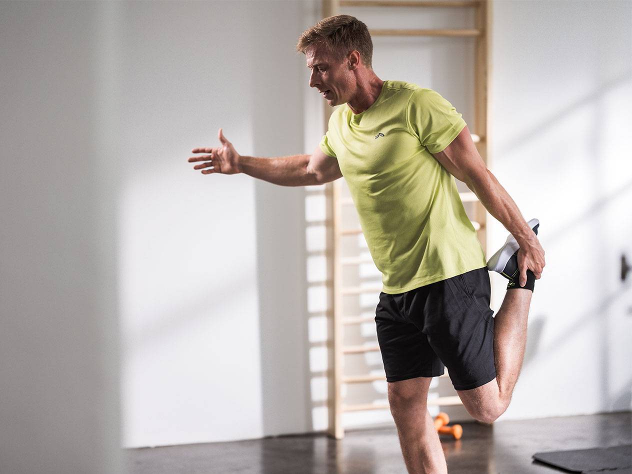 Homme s'étirant en short noir et t-shirt vert lime dans une salle de sport.