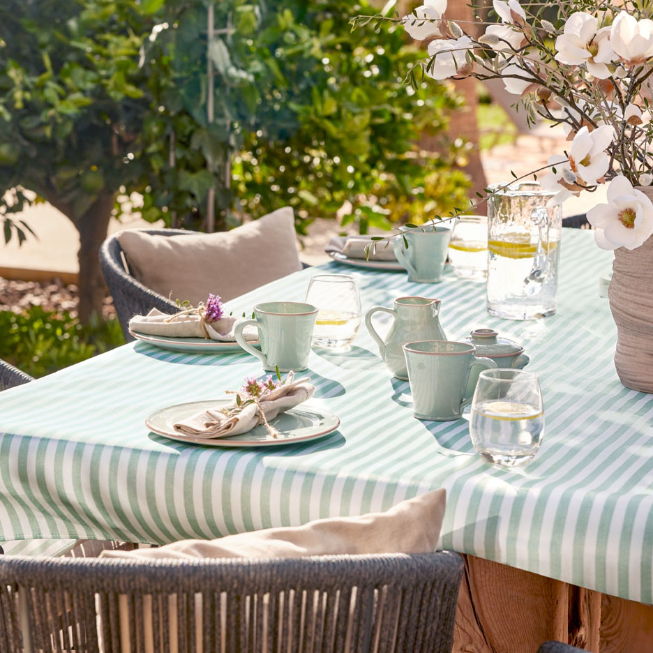 Gedekte tafel met servies en glazen op een groen gestreept tafelkleed op een terras.