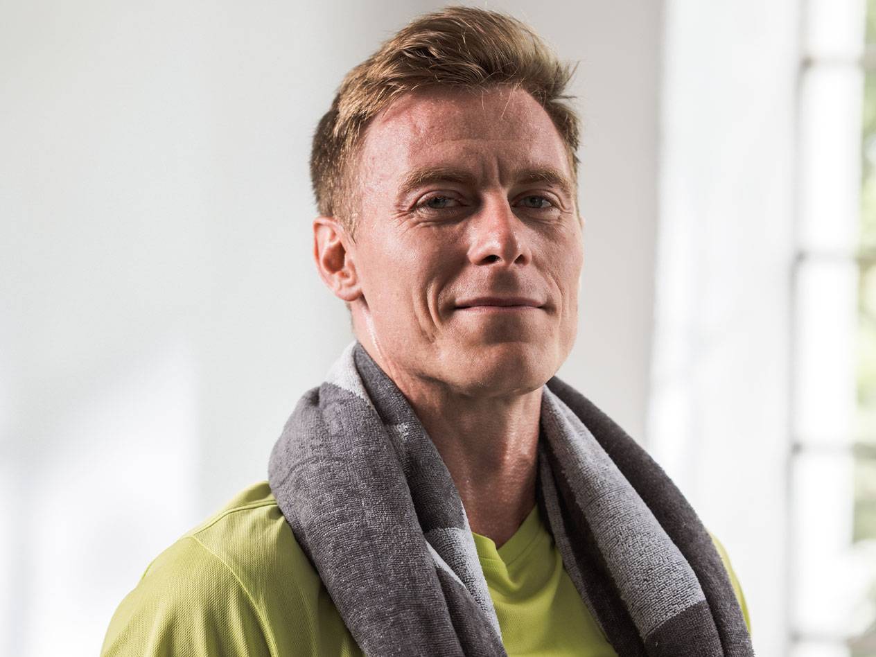 Un homme blond avec une serviette autour du cou regarde l'appareil photo.