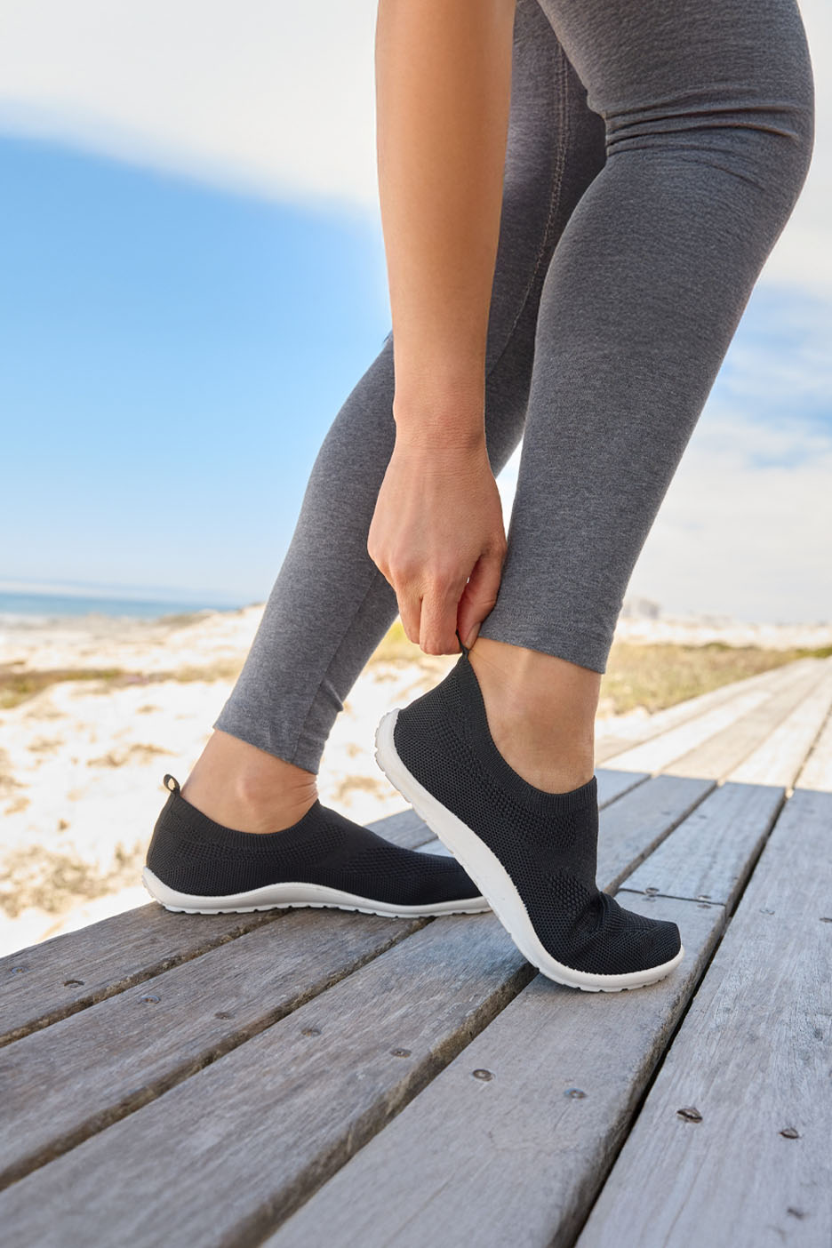 Een vrouw op het strand trekt zwarte gebreide sneakers aan.