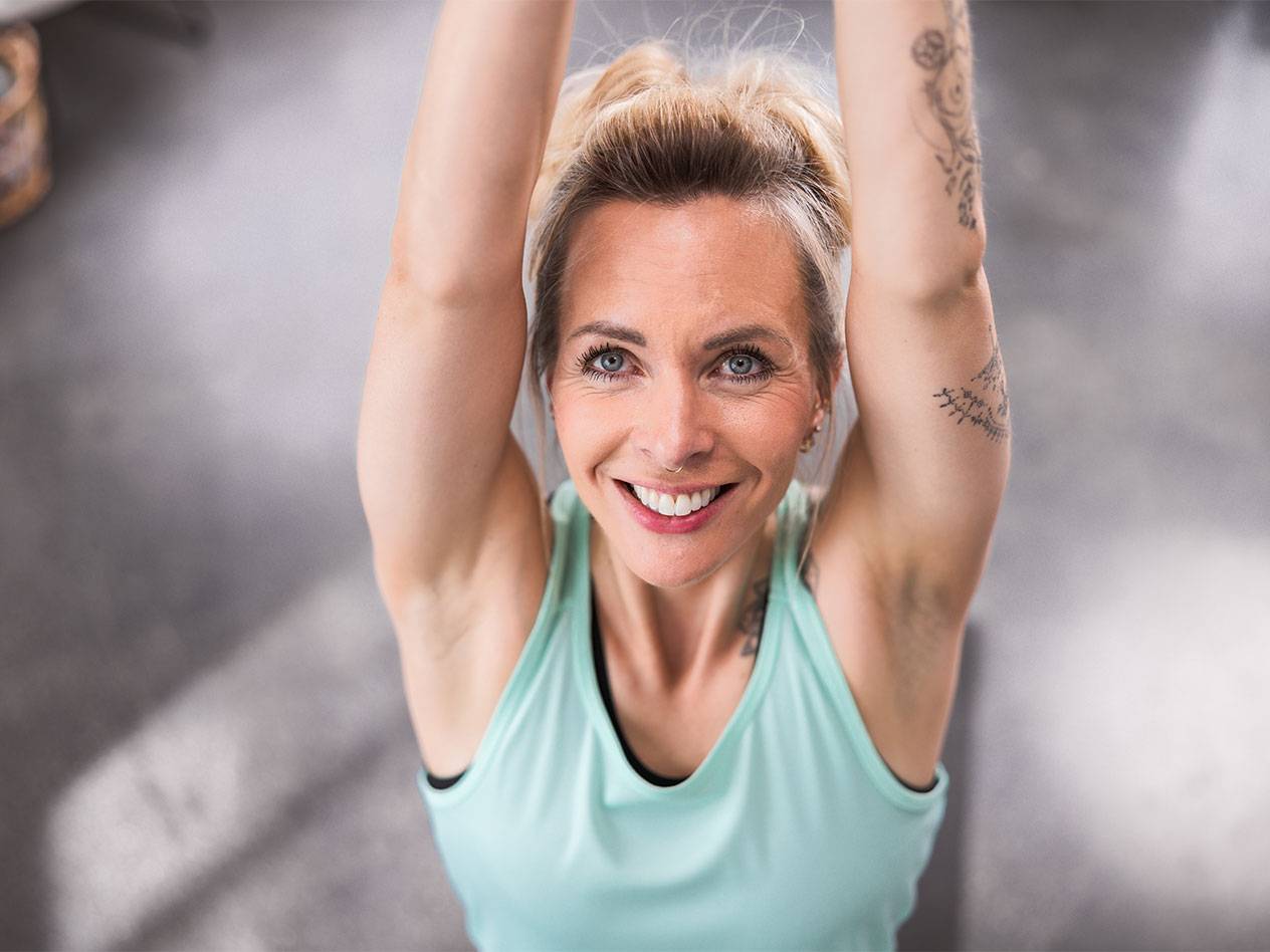 Femme blonde en débardeur bleu clair souriant à la caméra.