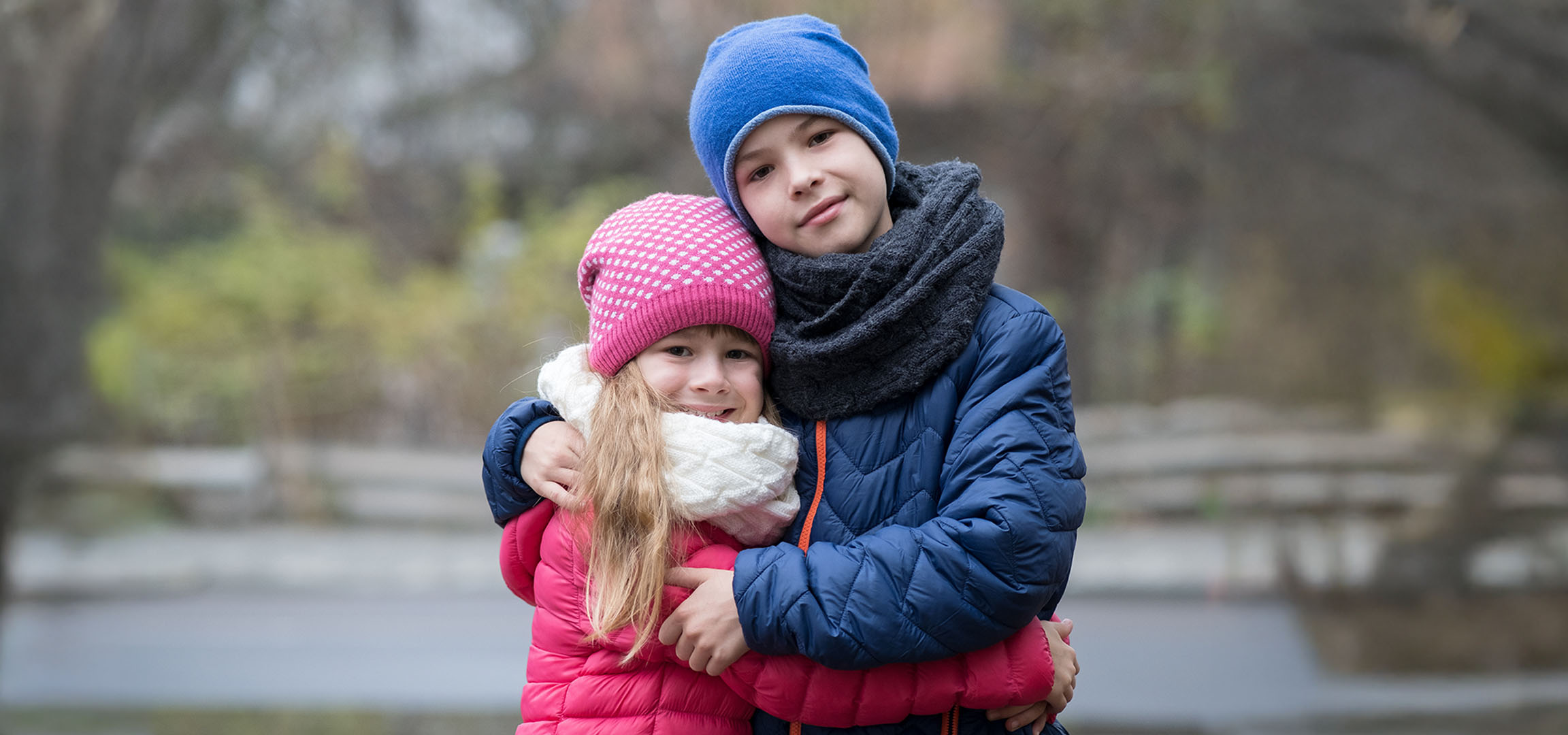 Deux enfants en bonnets et vestes d'hiver s'étreignent à l'extérieur.