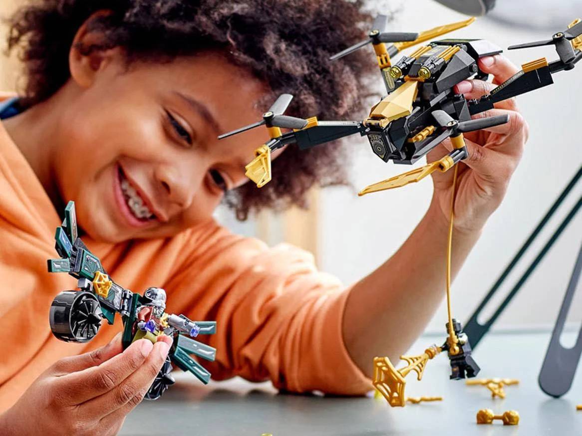 Lachend kind speelt met twee speelgoedvoertuigen en minifiguren.