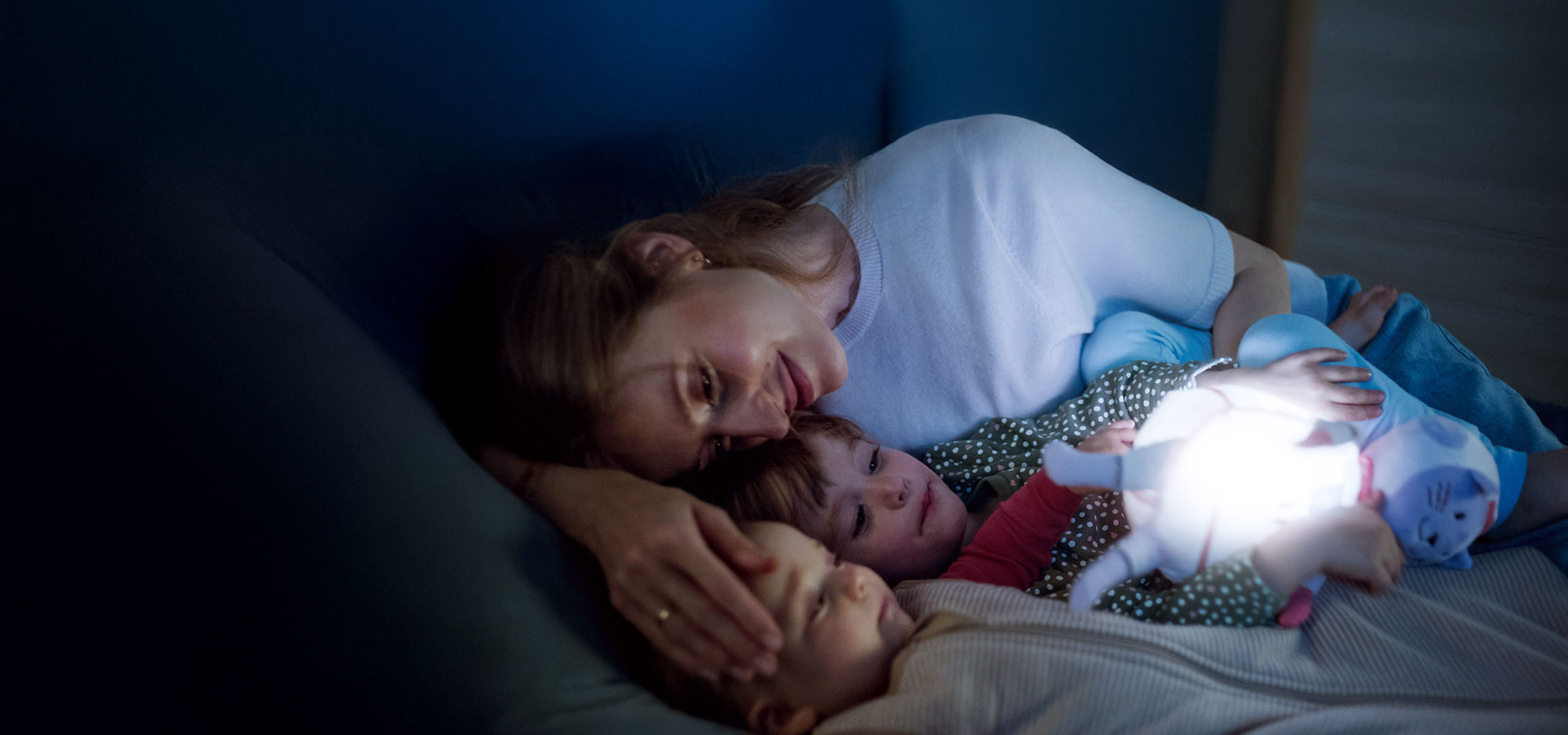 Maman et deux enfants au lit avec un jouet lumineux