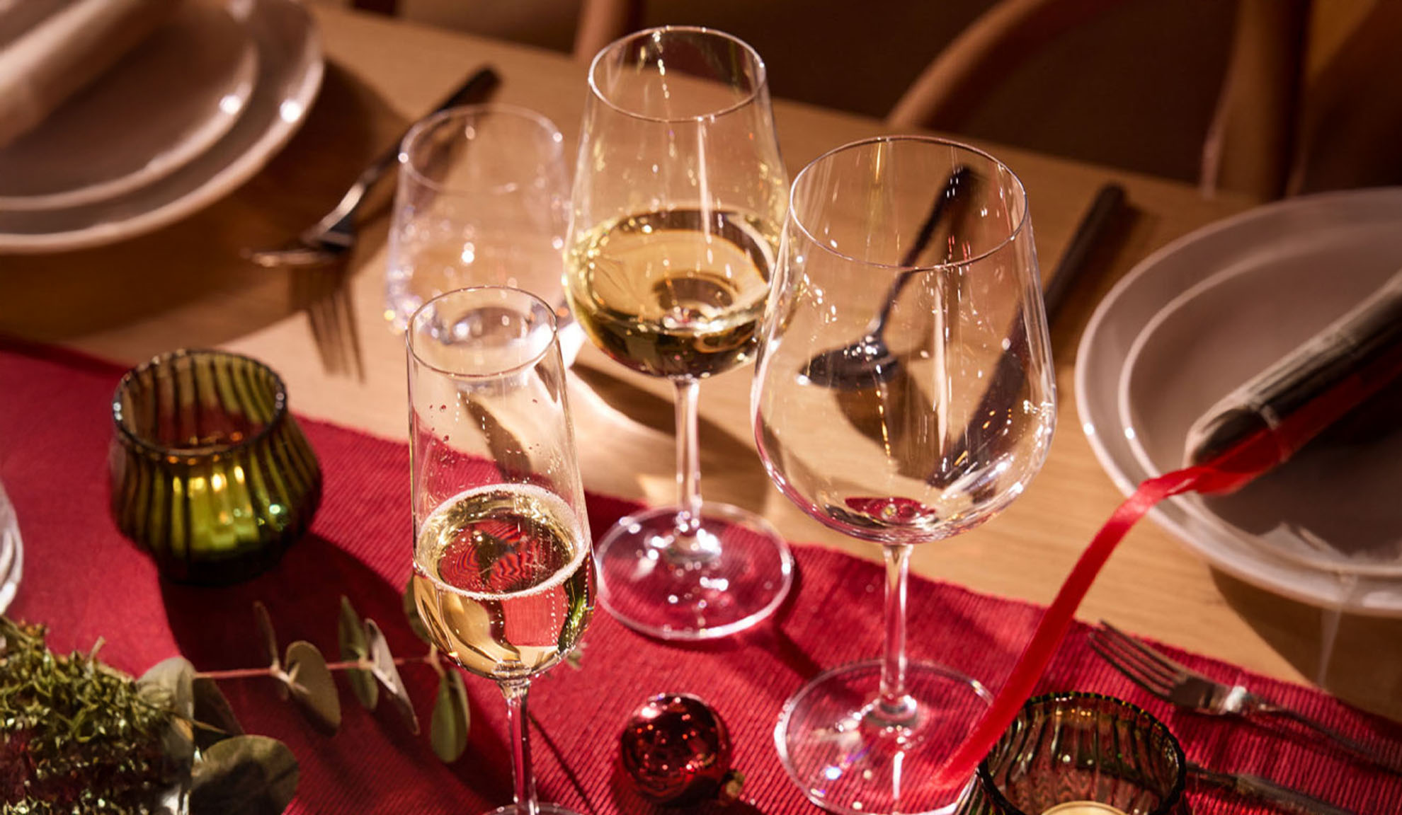 Feestelijk gedekte tafel met wijnglazen, champagneglas en kerstdecoratie.