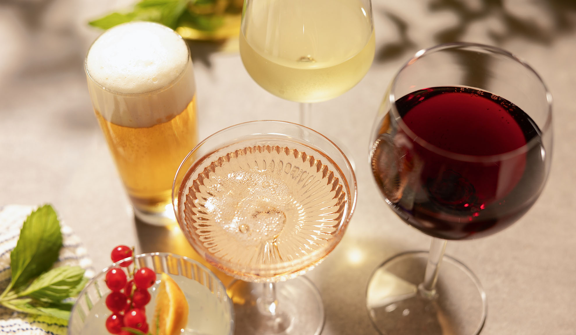 Verres de bière, vin blanc, rosé et rouge, avec un cocktail et des baies.