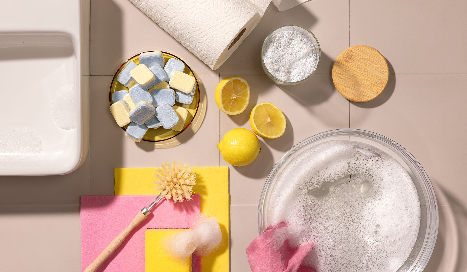 Produits de nettoyage : tablettes lave-vaisselle, citrons, poudre et éponges.