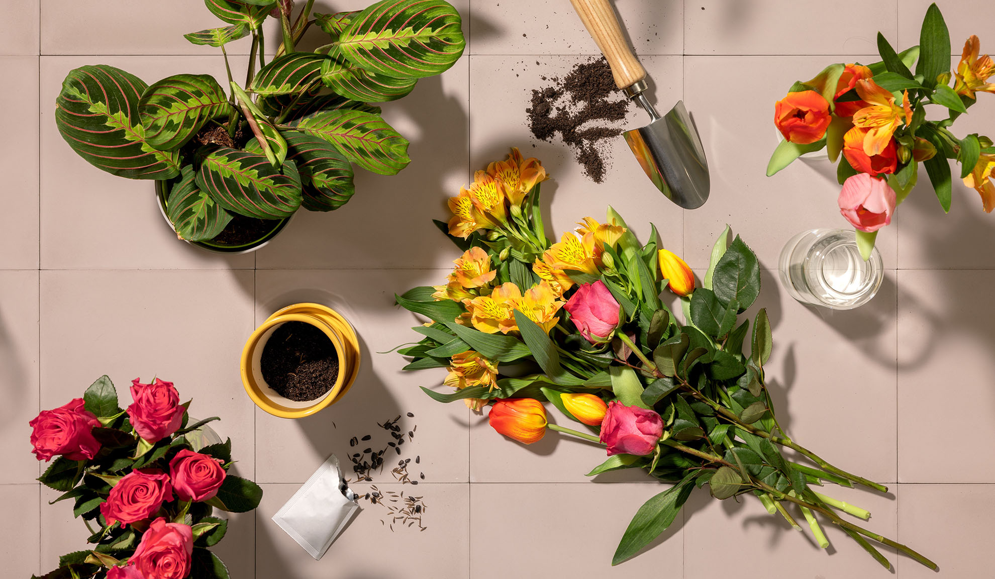 Bovenaanzicht van tuingereedschap, potplanten en boeketten kleurrijke bloemen op een tegeloppervlak.