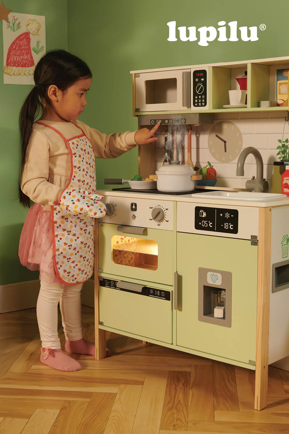 Een klein meisje speelt met een houten speelgoedkeuken met accessoires.