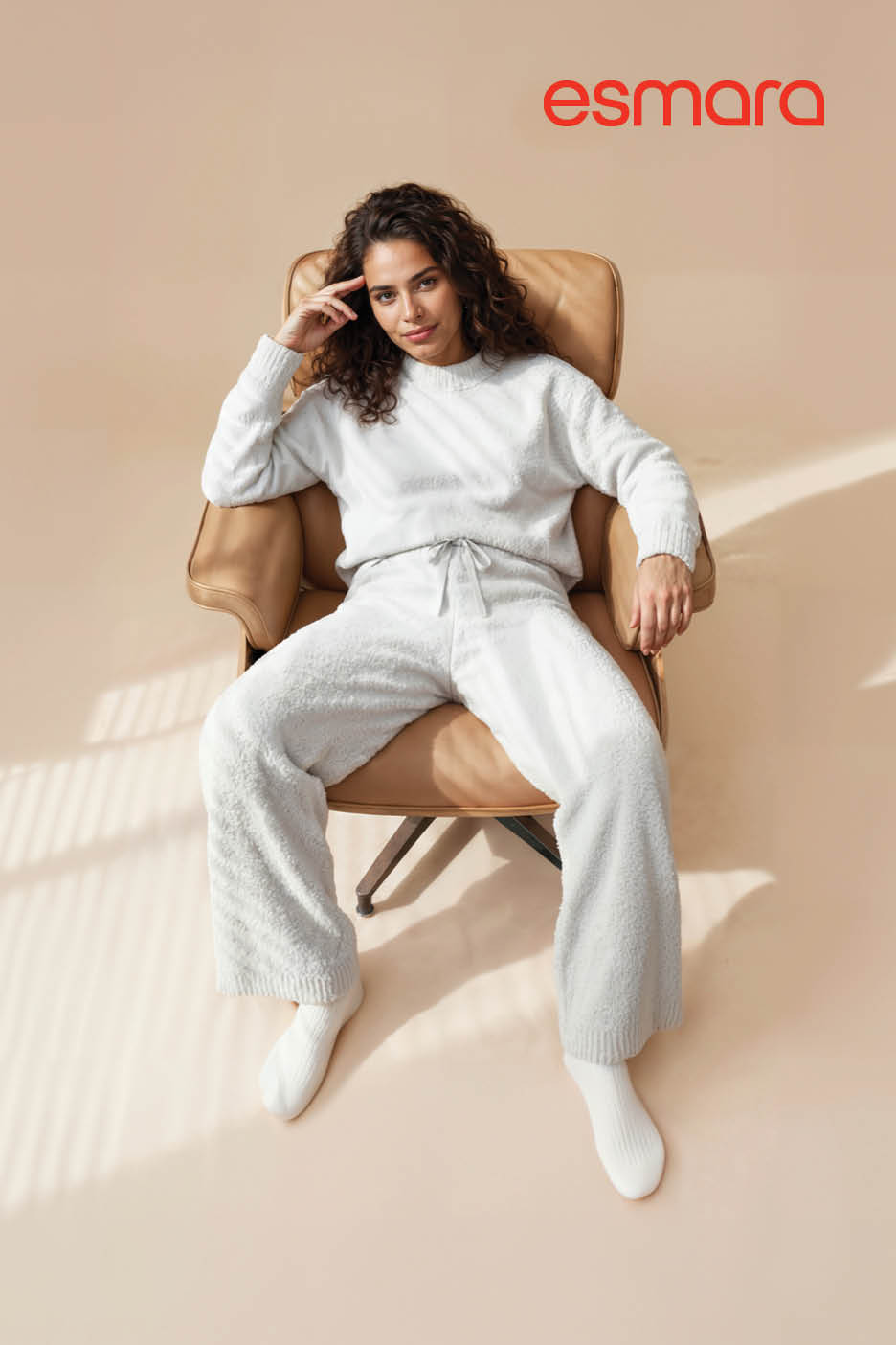 Een vrouw in een comfortabele witte loungewear set zit in een beige fauteuil.