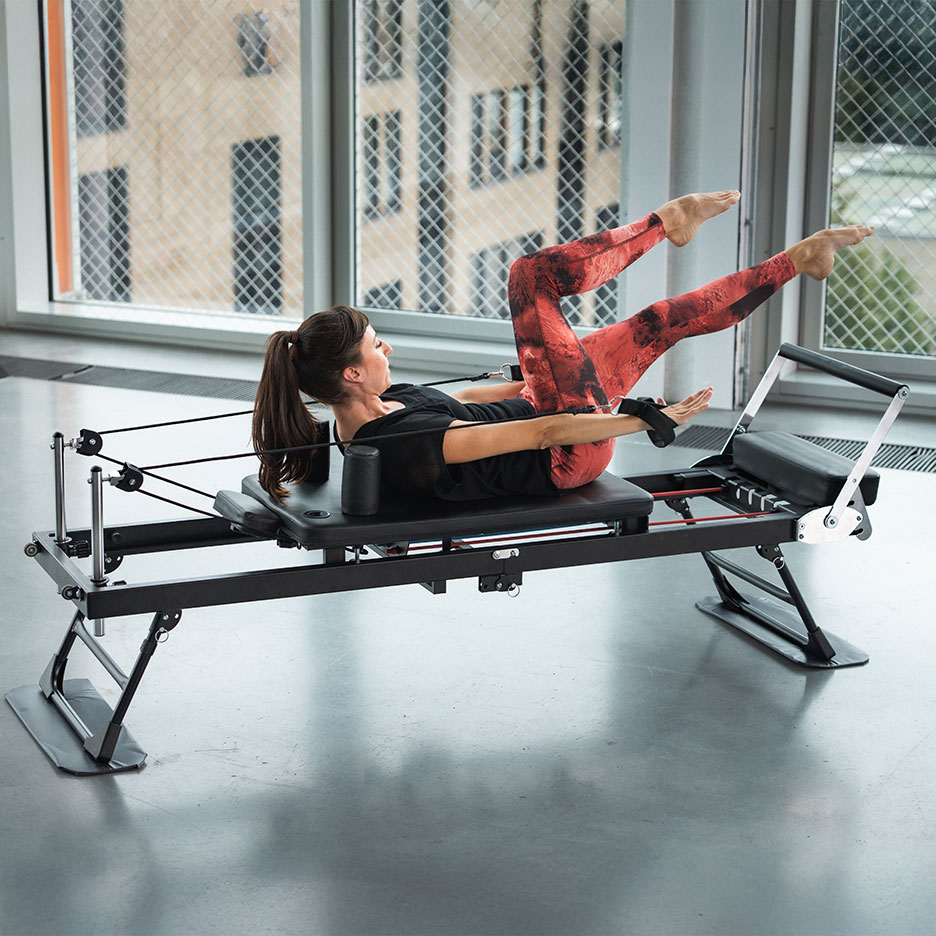 Vrouw doet Pilates op een reformer in een rode yogabroek.