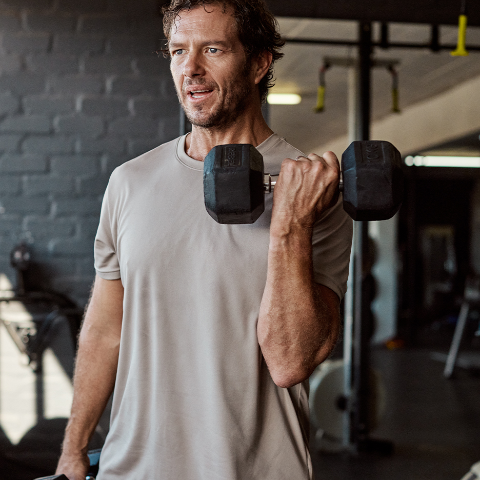 Man tilt een halter in de sportschool, draagt een sportshirt.
