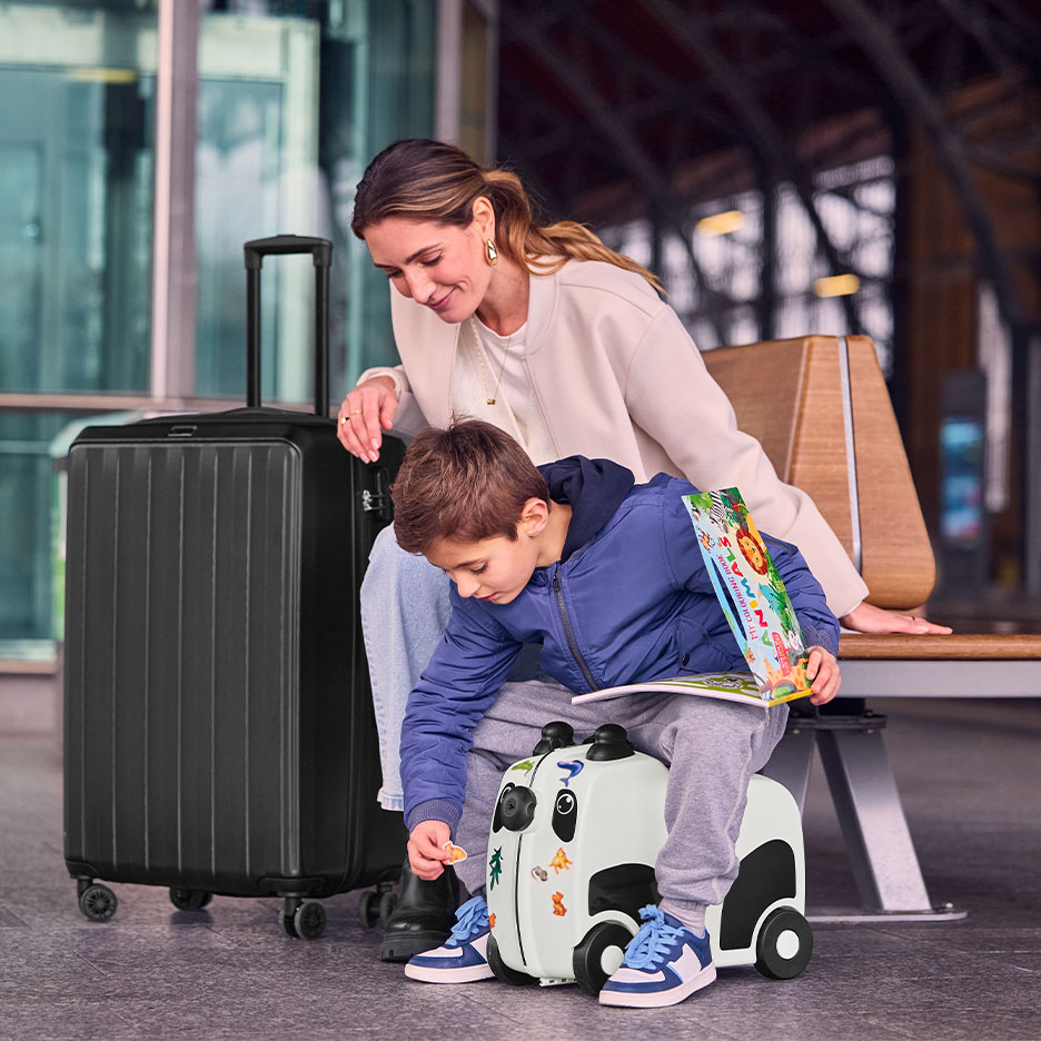 Vrouw en kind met grote zwarte koffer en panda-rijdkoffer op een luchthaven.