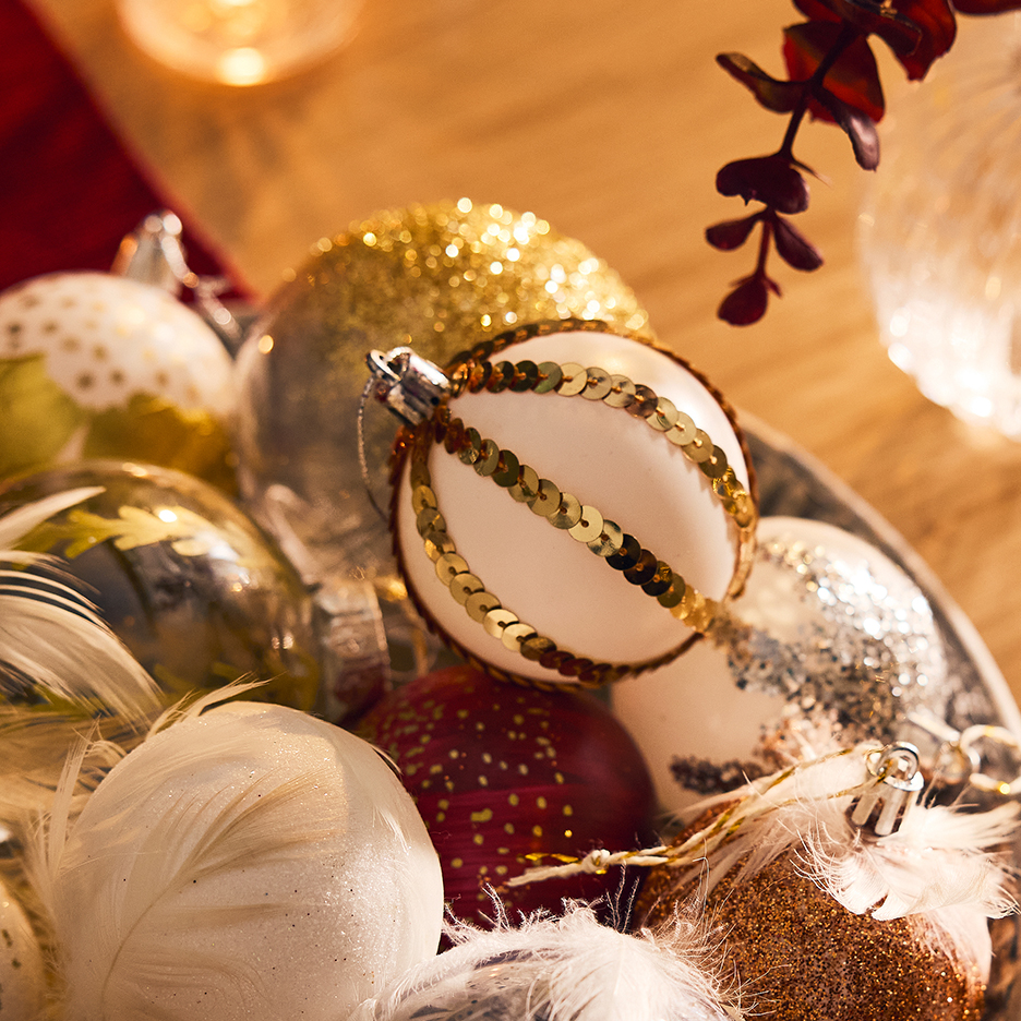 Een schaal met gouden, witte en rode kerstballen, met veren en pailletten.