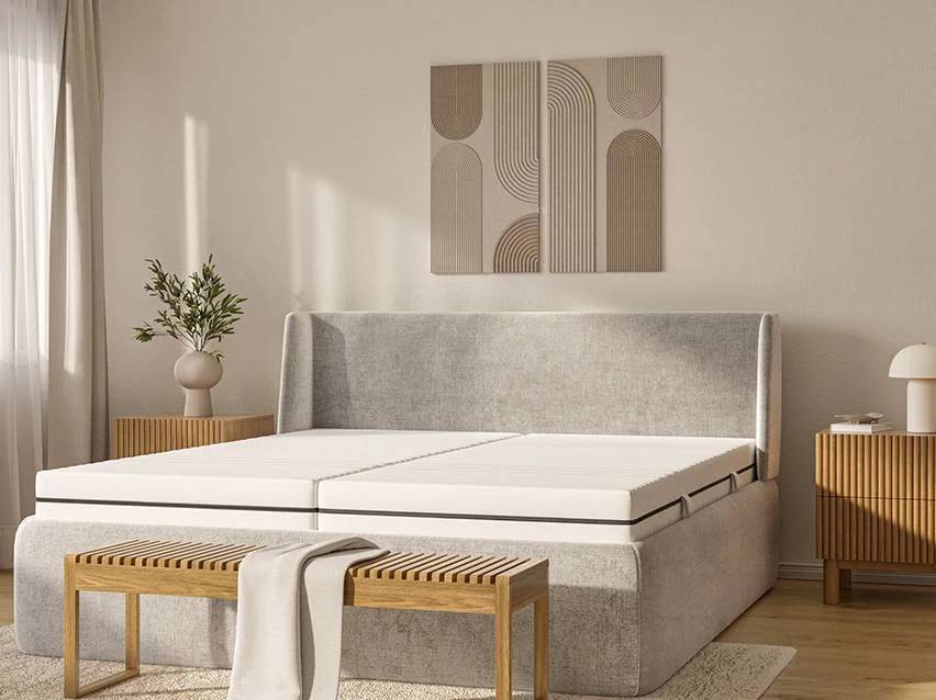 Een grijs bed met twee witte matrassen, een houten bankje en nachtkastjes.