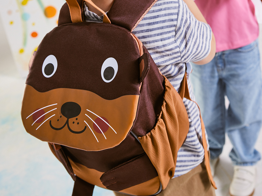 Un enfant porte un sac à dos en forme de loutre.