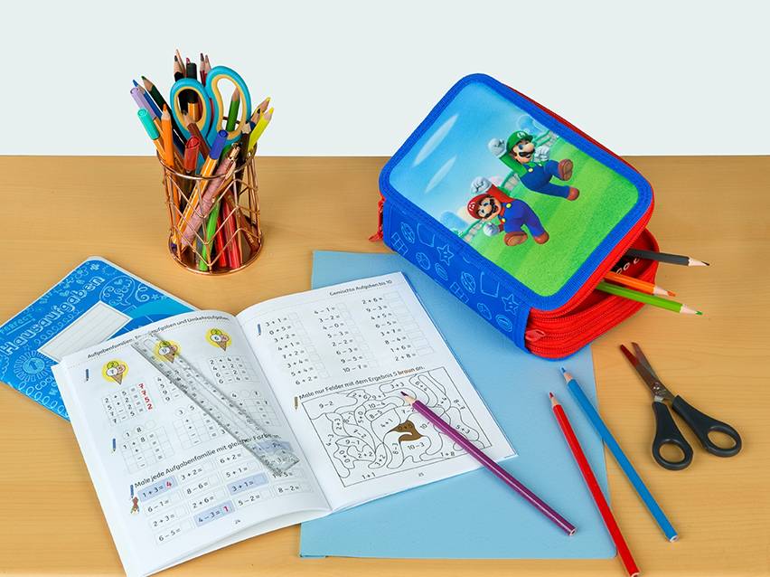 Een Super Mario etui, oefenboekjes en kleurpotloden op een tafel.