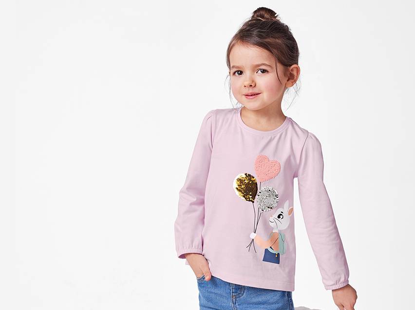Een schattig meisje draagt een lila longsleeve met paarse, gouden en zilveren ballon-applicaties.