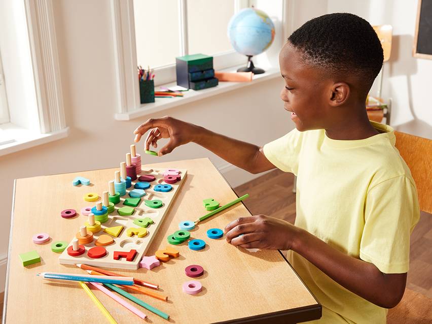 Een kind speelt met een houten sorteerspel met gekleurde ringen en vormen.