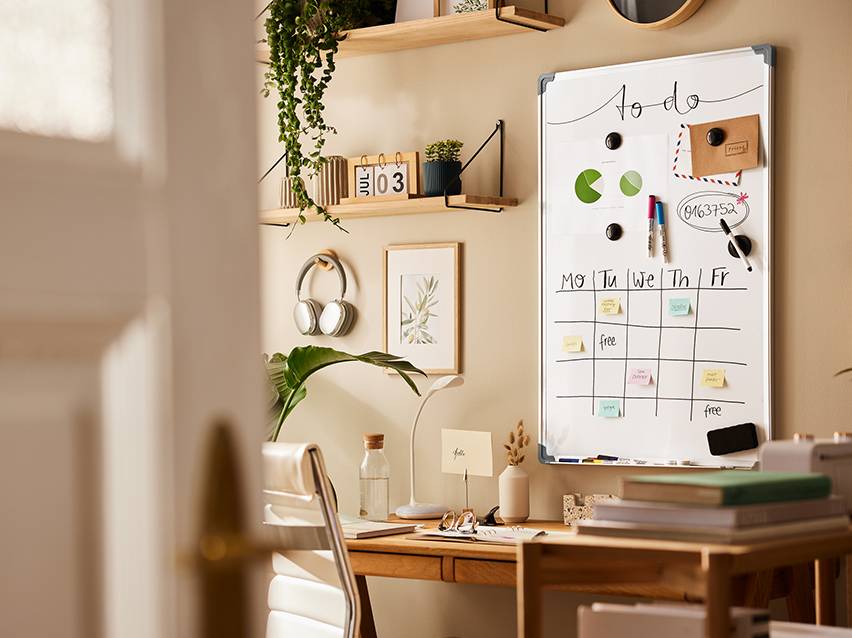 Een magnetisch whiteboard met een kalender en notities, in een georganiseerd kantoor met planten en kantoorartikelen.