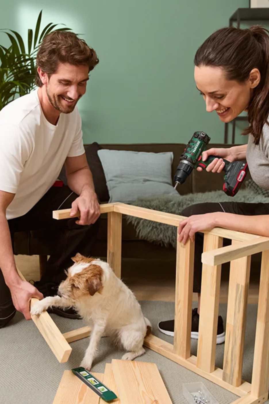 Een stel en hun hond monteren houten meubels met een accuboormachine.