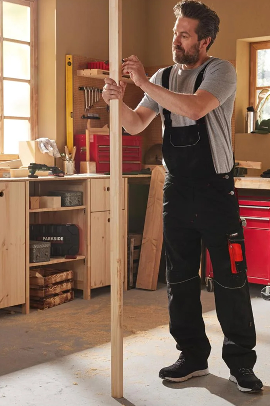 Een man in een zwarte werkoverall markeert een houten plank in een werkplaats.