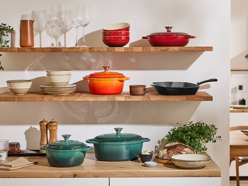 Keukenplanken met gietijzeren potten, pannen en serviesgoed in verschillende kleuren.