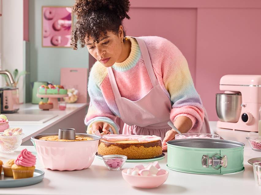 Een vrouw versiert taarten met roze en groene keukenbenodigdheden.