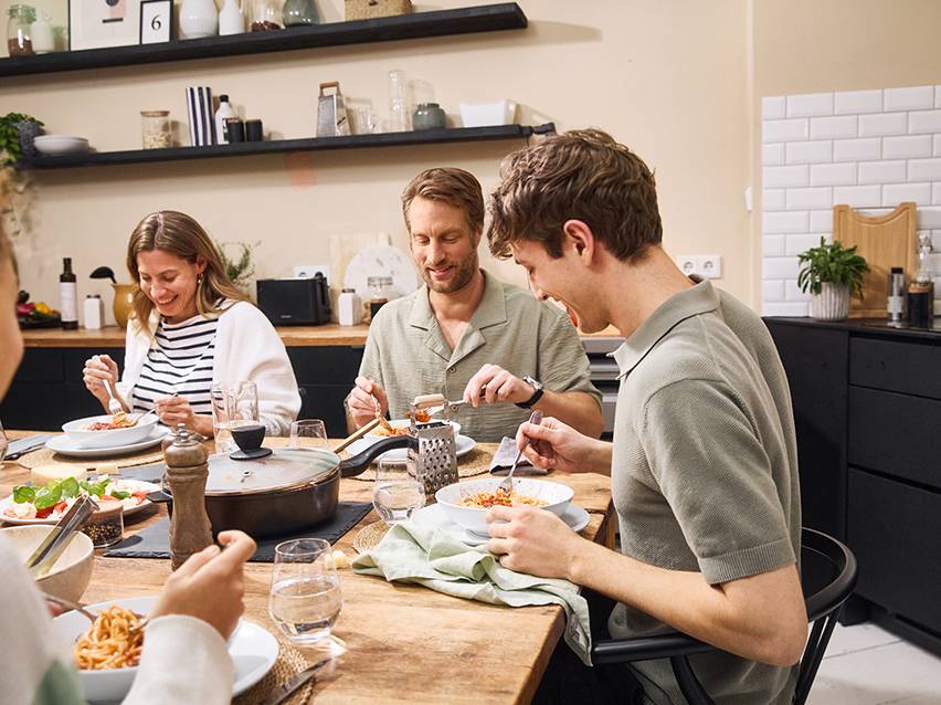 Vrienden delen een pastamaaltijd aan tafel in een moderne keuken.