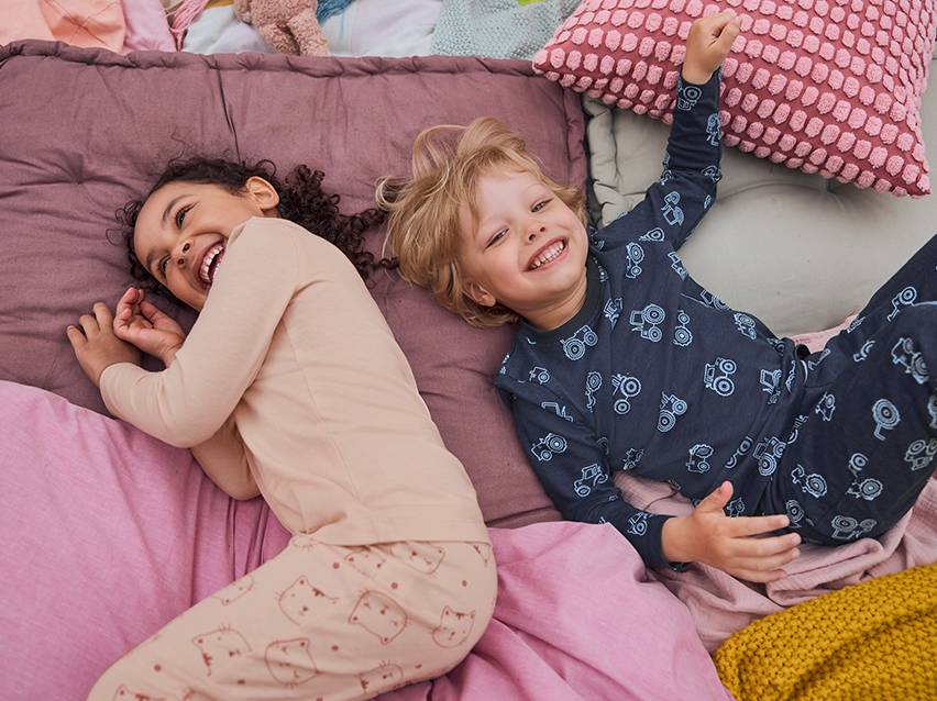 Twee lachende kinderen in pyjama op een knus bed.