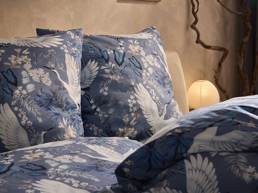Blauw beddengoed met witte kraanvogels en bloemen in een slaapkamer.