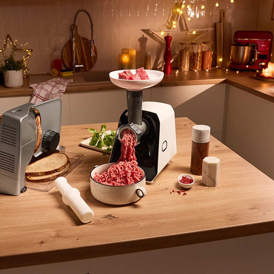 Keuken met vleesmolen, broodsnijmachine en keukenmachine, versierd met kerstverlichting.