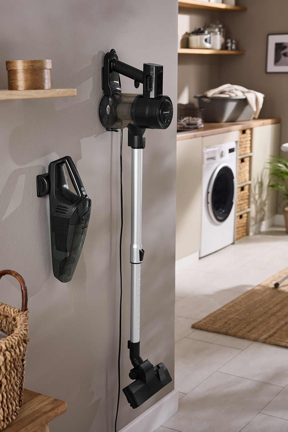 Twee aan de muur gemonteerde stofzuigers in een bijkeuken met wasmachine en strijkplank.