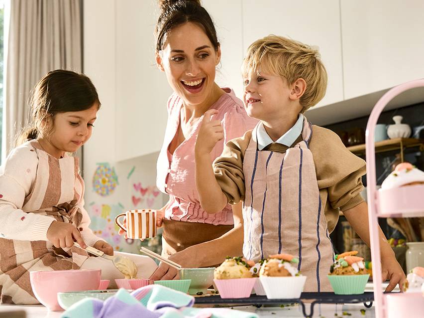 Mère et enfants préparant des cupcakes colorés dans une cuisine lumineuse.