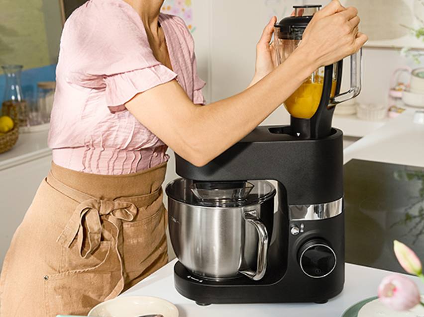 Een vrouw gebruikt een zwarte keukenmachine met een roestvrijstalen mengkom en een blender.