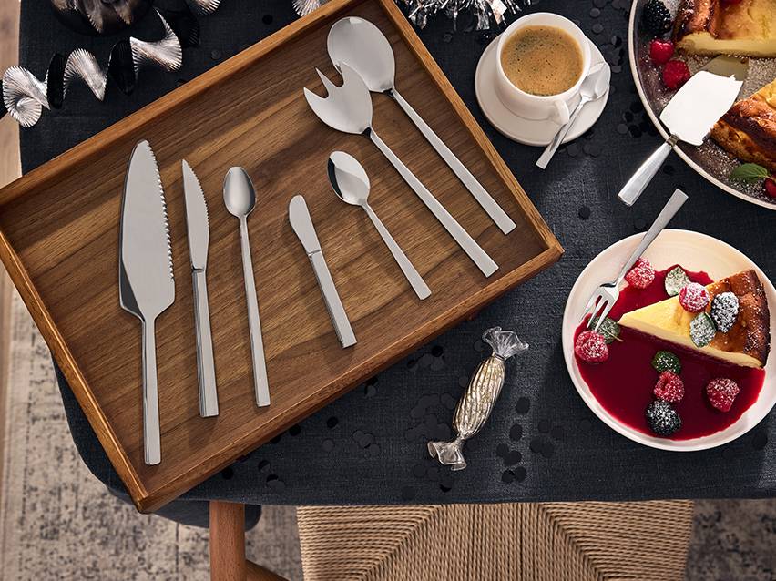 Roestvrijstalen serveerbestekset op een houten dienblad, met cheesecake en koffie.